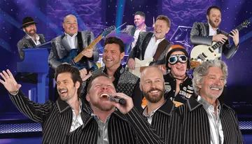 A group of performers, dressed in sparkly outfits, are enthusiastically singing and playing instruments on stage.