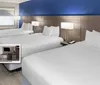 The image shows a modern hotel room with three beds a blue accent wall and amenities including free hot breakfast an outdoor pool and free Wi-Fi