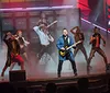 The image captures a dynamic stage performance with dancers and a guitarist accompanied by glowing reviews from Norbert and Bambi