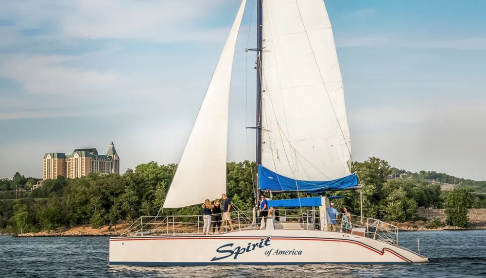 A group of people enjoys a sunny day sailing on a boat named Spirit of America with a backdrop of a lakeshore and buildings