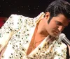 A performer in a bejeweled white suit is singing into a microphone on stage