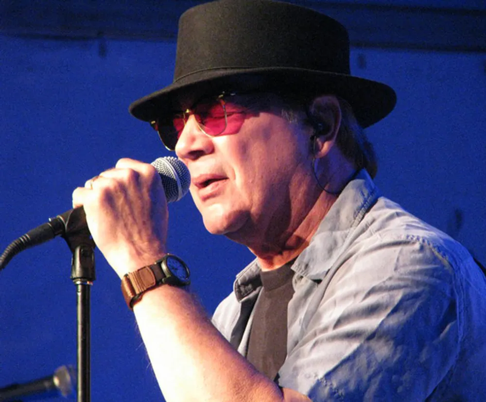 A man wearing a black hat and red sunglasses is performing into a microphone