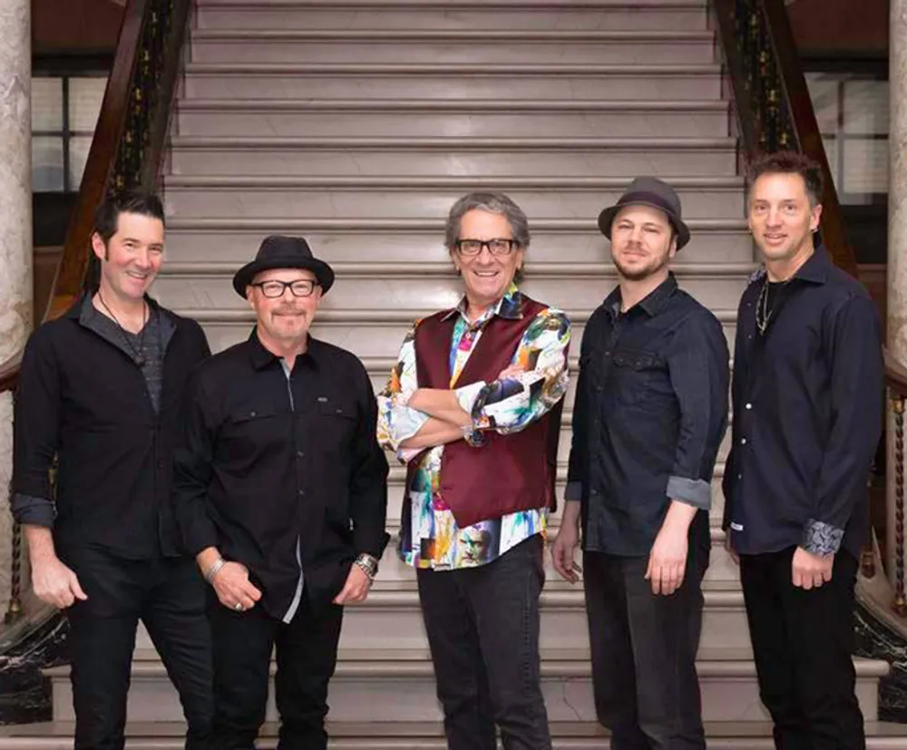 Five men are standing on a staircase posing for a group photo with four of them dressed in black and one in a colorful shirt