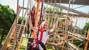 A group of people is enjoying a high ropes adventure course on a sunny day.