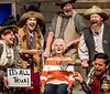 The image depicts a lively scene with five people dressed in Western-style costumes at a dinner theater expressing exaggerated emotions of joy alongside a quote saying Food was WONDERFUL above a picture of a meal