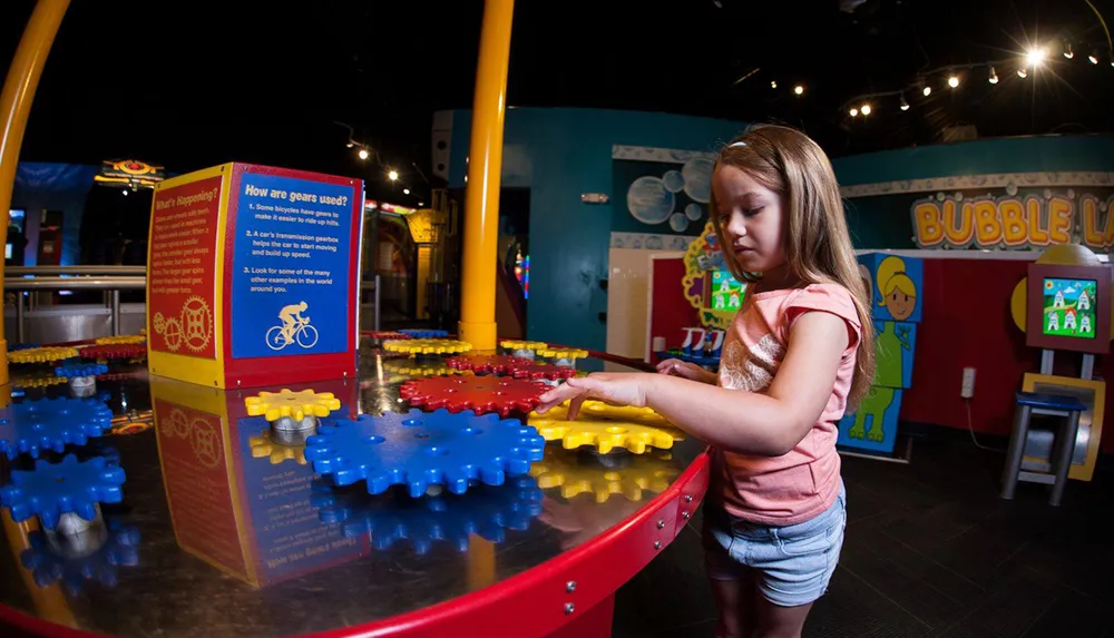 A young girl is engaged with an interactive exhibit involving colorful gears at a childrens museum