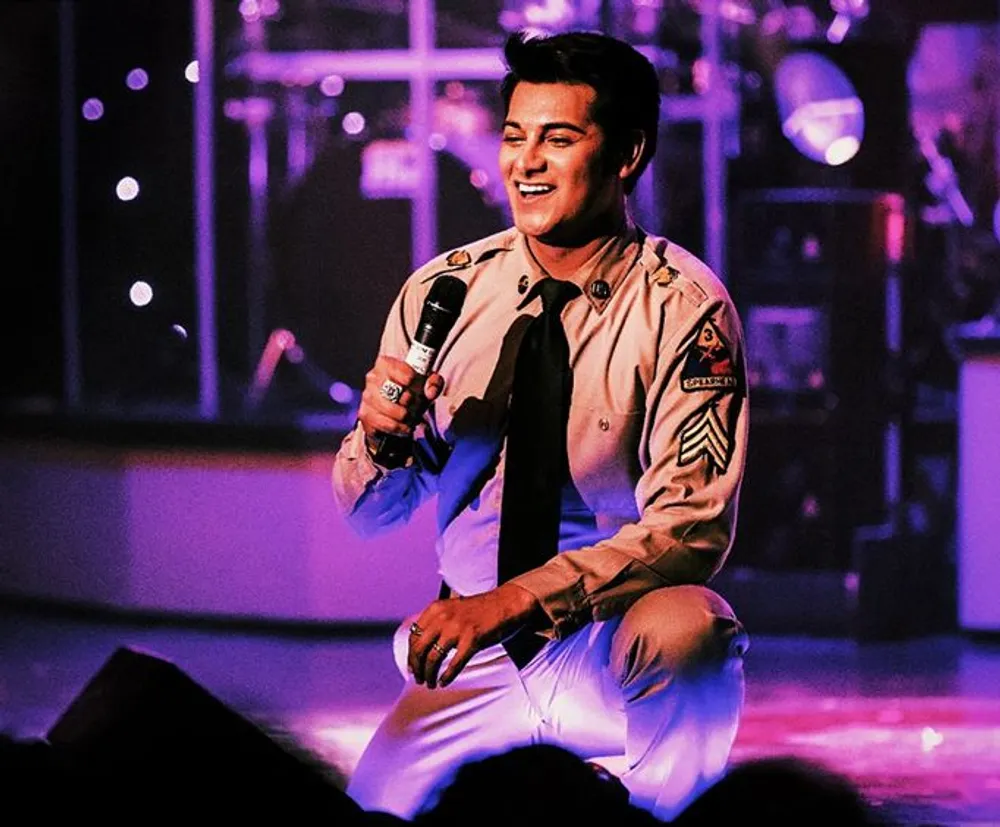 A performer dressed in a vintage military-style uniform is singing with a microphone squatting on stage with a smile under colorful stage lighting