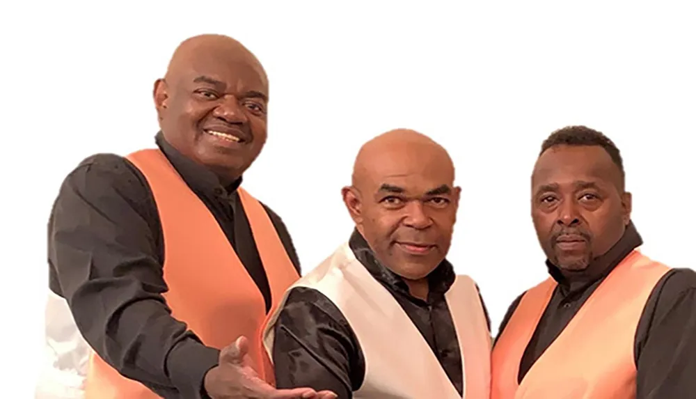 Three men in matching black and orange vests are posing together for a photo with one slightly in front of the other two all looking directly at the camera