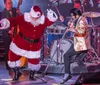 A person dressed as Santa Claus is energetically dancing on stage with a singer in a shiny gold jacket