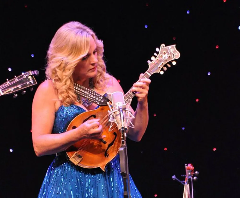 A woman in a blue dress is playing a mandolin on stage under illuminated lights