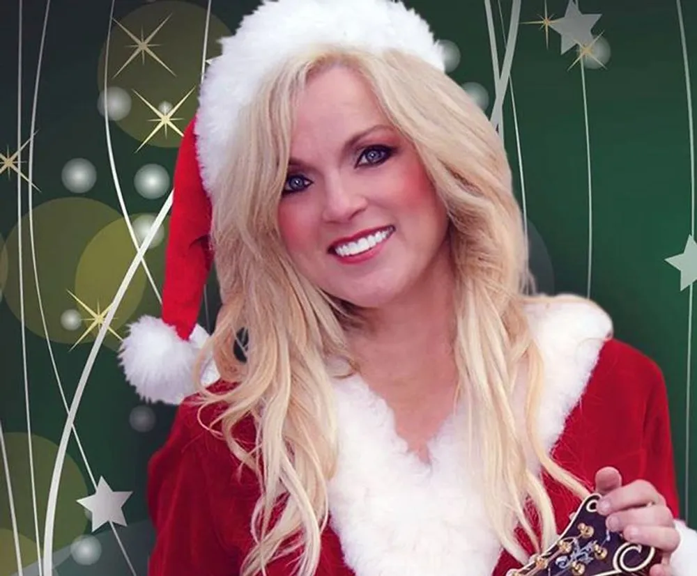 A woman is smiling for the camera dressed in a Santa Claus outfit against a festive background with green hues and golden stars and circles