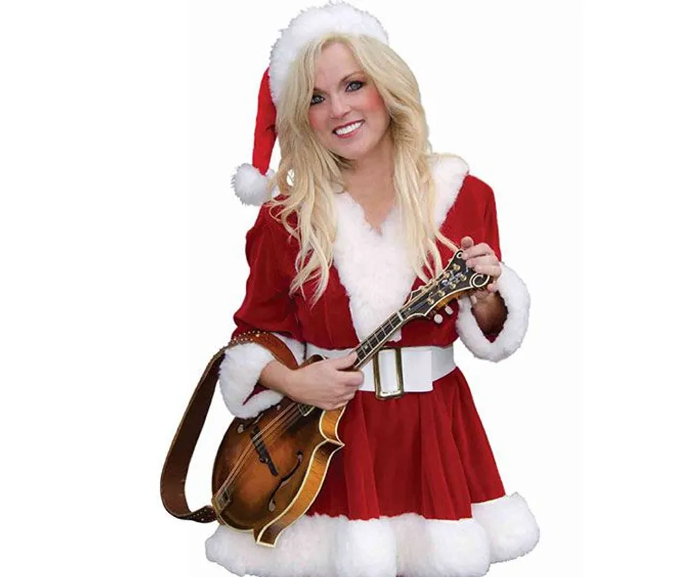 A person is dressed in a festive Santa-inspired outfit holding a mandolin and smiling