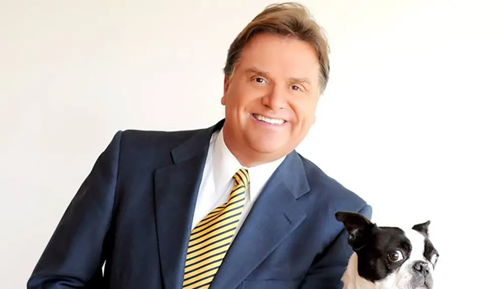 The image shows a smiling man in a suit and tie posing with a Boston Terrier dog