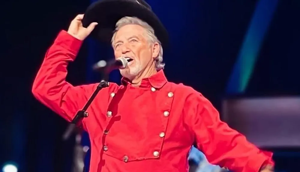 A person in a red outfit and black hat is performing on stage while singing into a microphone