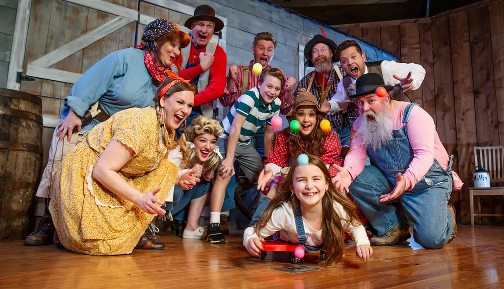 A group of exuberant people in various colorful and characterful costumes pose playfully on a wooden stage likely during a theatrical production or costume party