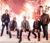 Five men wearing winter clothing are posing in front of a snowy illuminated street scene