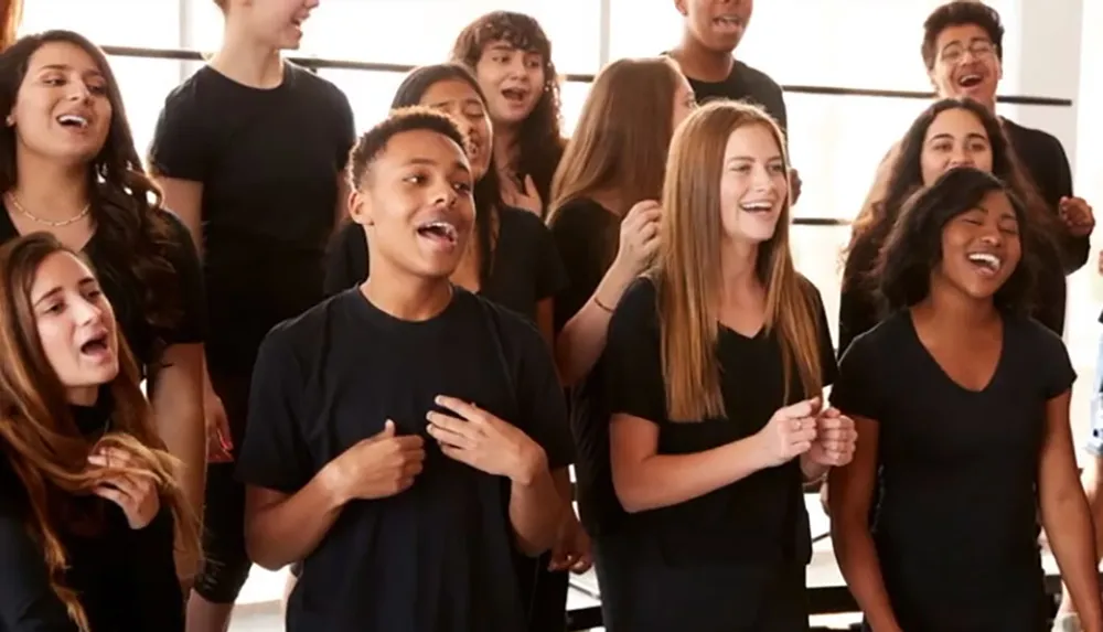 A group of joyful students is singing together with some placing their hands over their hearts