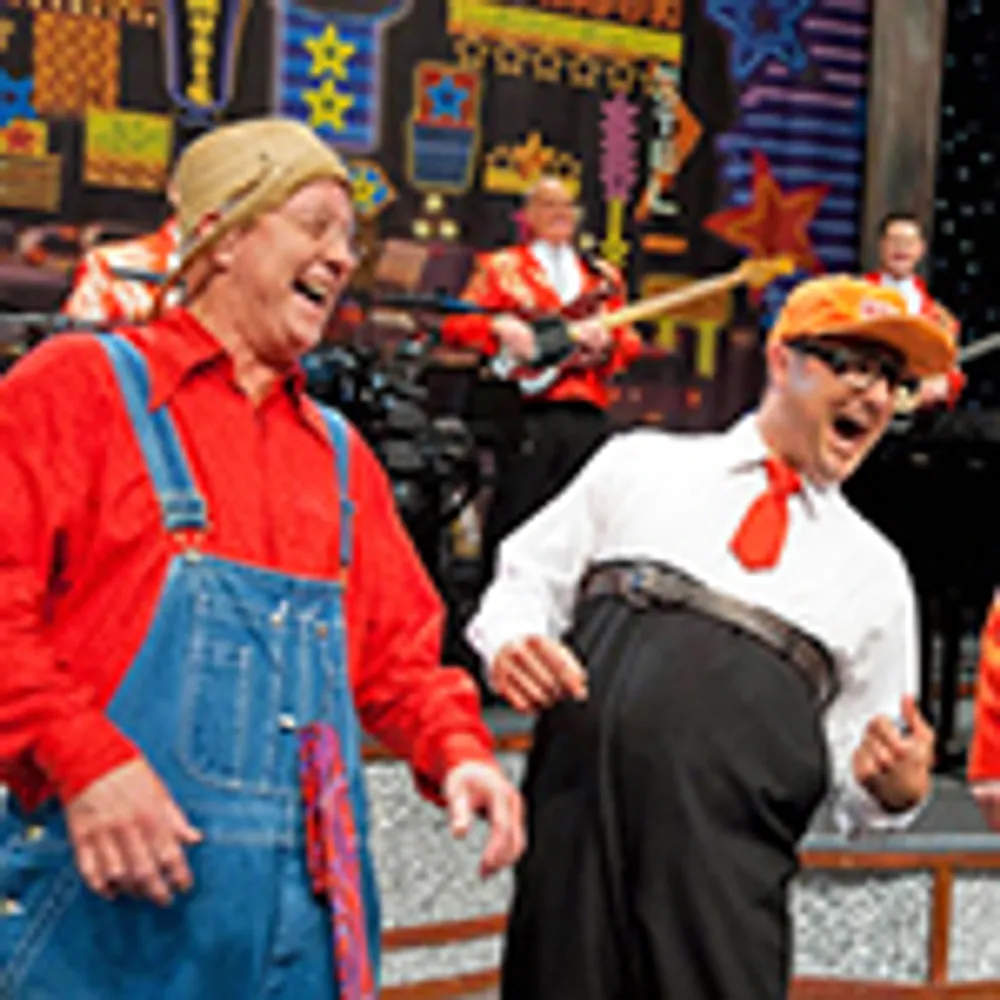 Two people are dressed humorously laughing and having fun on a festive stage