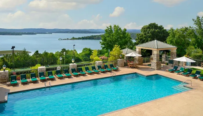 An outdoor swimming pool with loungers overlooks a scenic lake offering a tranquil recreational space