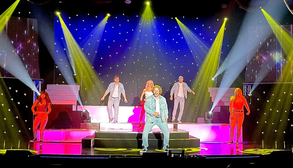 Performers are dancing on a brightly lit stage with a backdrop of star-like lights