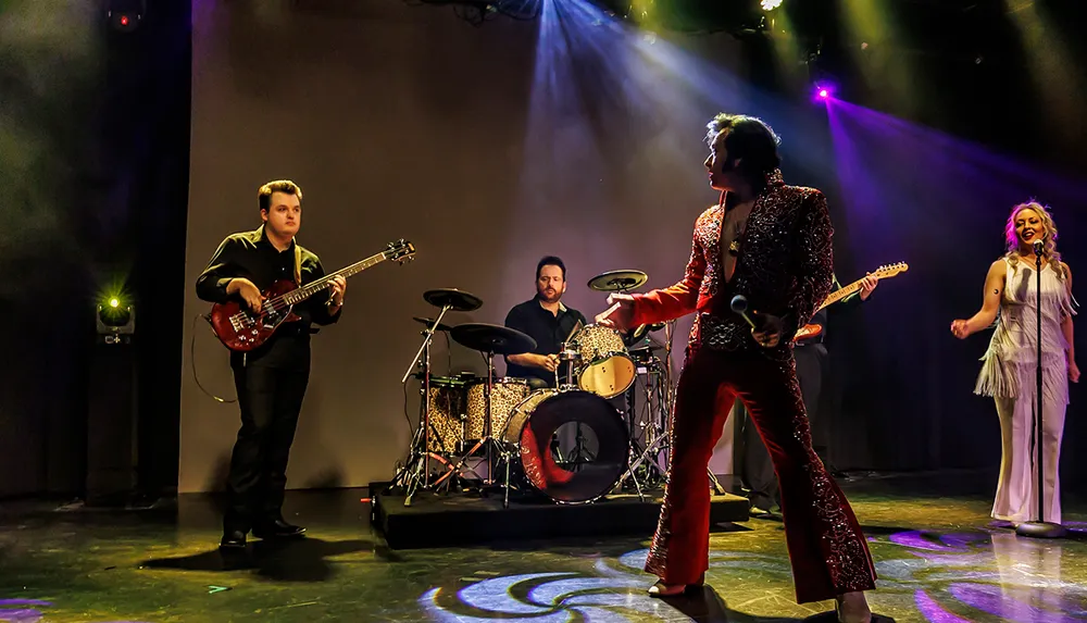 A live performance on stage features a singer in a sparkly outfit surrounded by a band including a guitarist drummer and backup vocalist under colorful lighting