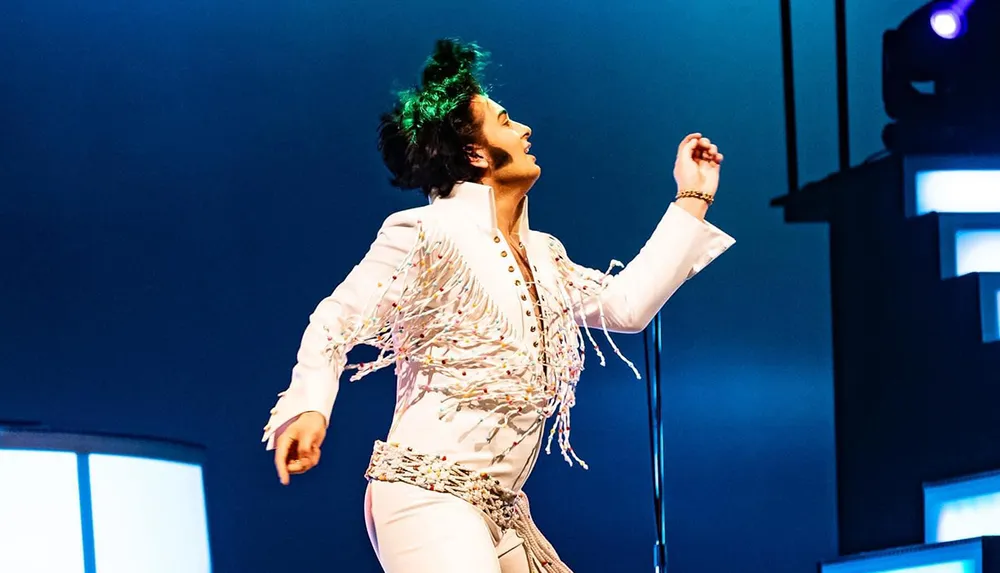 A person energetically performs on stage wearing a white fringed outfit